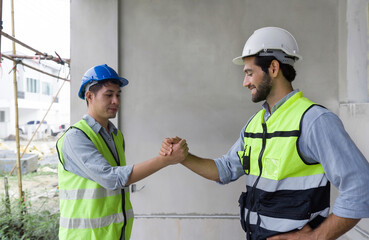 Two construction workers in safety vest and helmet join hands together on a construction site, showing teamwork and agreement.