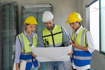 Young caucasian foreman in helmet and safety vest look at the construction plan. Work environment at construction site of housing project.