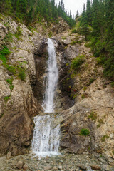 Fototapeta premium Majestic waterfall cascading down rugged rocks. Surrounded by lush forest, popular hiking spot. Picturesque scenery, travel destination, tourist attraction. Outdoor adventure, serene landscape.