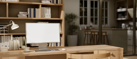 A computer with a white-screen mockup with decor are on a wooden desk in a minimalist home office. © bongkarn