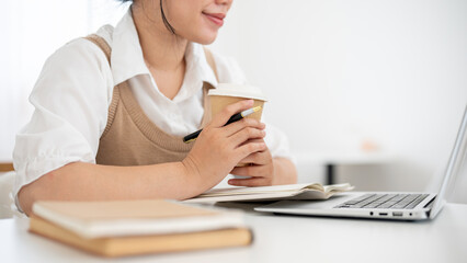 Fototapeta premium A cropped image of a woman working remotely from a coffee shop, reading something on her laptop.