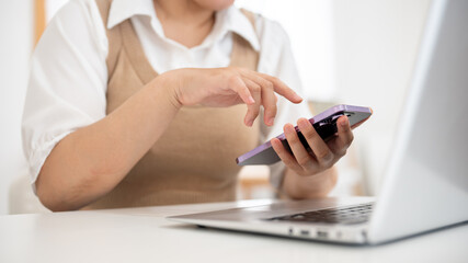 A close-up image of a woman using her smartphone at her desk in a minimal white room.