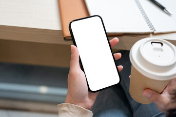 A woman sitting at an indoor table with her books, sipping coffee, and using her smartphone.