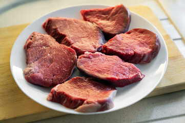 Uncooked beef steaks are laying on a white plate