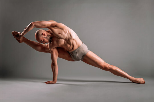 Athletic male dancer performing splits and holding foot in studio
