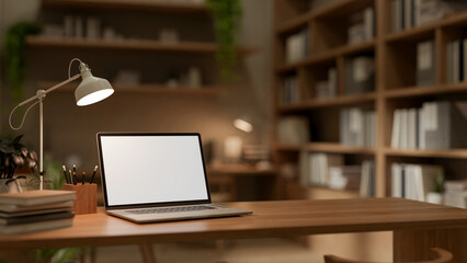 A close-up image of a laptop computer and stationery on a wooden table in a cozy office room.