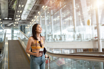 An attractive, happy Asian female tourist passenger with her belongings is on the airport escalator.