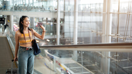 A gorgeous young Asian female tourist passenger is on an airport escalator, carrying her luggage.