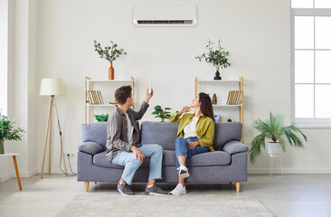 Young married couple relaxing sitting on couch and enjoying their new modern air conditioning...