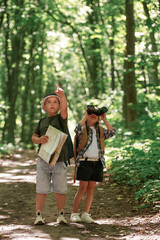 Checking the way on the map. Kids in forest at summer daytime together