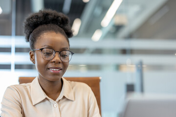 Confident businesswoman wearing glasses working on laptop in modern office environment. Business professional focused on work, embodying productivity, confidence, professionalism workplace setting.