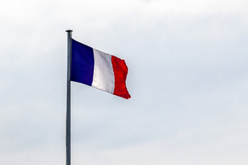 French flag blowing in the wind, atop a metal pole, against clear sky, providing copy space.