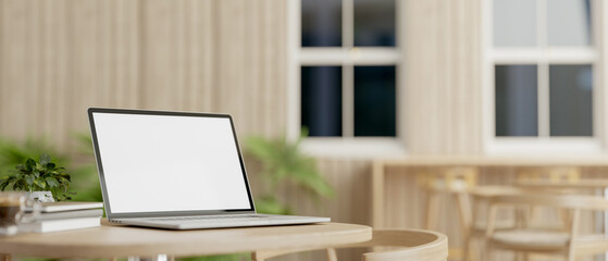 A laptop computer with a white-screen mockup on a table in a comfortable minimalist cafe.