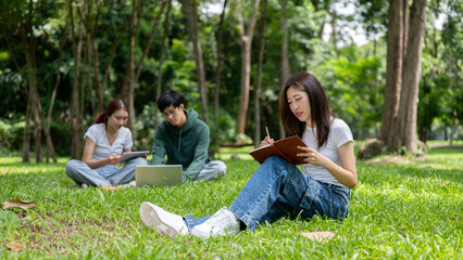 A young Asian female college student is doing homework or writing her diary in the campus park.