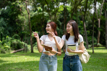 Two happy young Asian female college students with backpacks are walking in the park together.