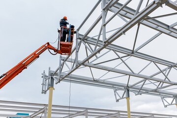 Fototapeta premium Man worker on a crane performs high-rise work on welding metal structures of new tower at height