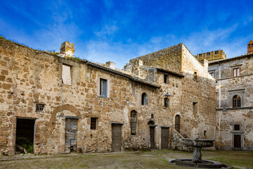 Obraz premium A glimpse of the ancient medieval village of Montecalvello, Viterbo, Italy. The internal courtyard of the castle with the ancient stone and brick buildings and the fountain in the center.