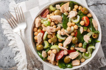 Mediterranean tuna chickpea salad with tomatoes, spinach, celery and olives dressed with vinaigrette close-up in a bowl on the table. Horizontal top view from above