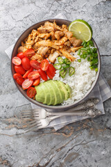 Mexican rice bowl with chicken carnitas, cherry tomatoes, avocado, peppers close-up on the table. Vertical top view from above