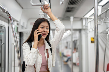An Asian female tourist is holding a handrail and talking on the phone while taking a sky train.