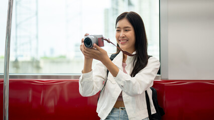 An Asian female tourist is taking pictures with her camera while commuting in a city on a sky train.