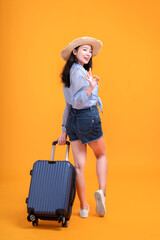 Happy young Asian tourist woman holding baggage going to travel on holidays isolated on orange background.