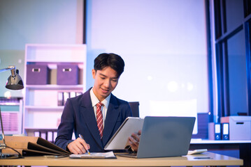 Fototapeta premium Businessman drinking coffee to get some energy for working overtime sitting at desk using computer and doing overtime