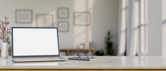 Fototapeta premium A laptop computer mockup, eyeglasses, and a book on a white marble table in a minimal white room.