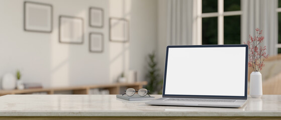A laptop computer mockup, eyeglasses, and a book on a white marble table in a minimal white room.