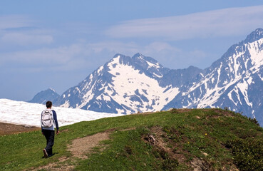 Fototapeta premium Man with backpack walks along hiking trail in mountainous area. Hiking concept.