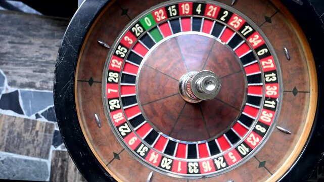 A close-up shot of a vintage roulette wheel spinning in a casino setting. The wheel is made of wood and metal and features a classic design