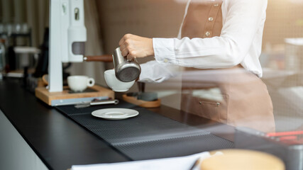 A close-up image of a female barista pouring milk into a coffee cup, working in a coffee shop.