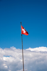 swiss flag on a long pole with the blue sky and cumulus clouds