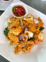 Omelette with shrimp and seafood on rice and sauce on white ceramic plate and spoon and fork.