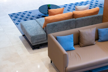 Comfortable modern brown and grey sofa with full color pillows and table on carpet, top view.