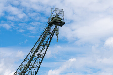 A tall industrial port crane extending towards the sky, set against a backdrop of scattered clouds.