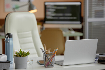 Background shot of empty modern office workspace with desk and chair, laptop and stationery at IT company, copy space