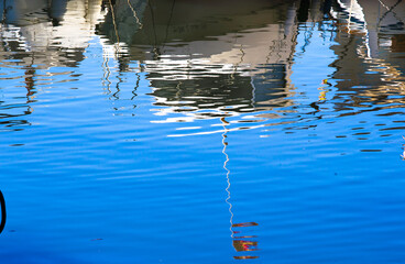Reflection of boats and a tattered Spanish flag in clear blue water, with ripples creating an abstract effect