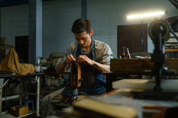 Young leather craftsman carefully stitching leather pieces. Small business and handmade concept