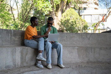 Focused couple of black students studying outside using laptop. Serious concentrated African American girl, guy work together on educational project, doing homework, prepare for classes at university
