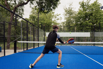 Young man in action playing padel tennis on an outdoor court. The player is focused and engaged, showcasing athletic performance.