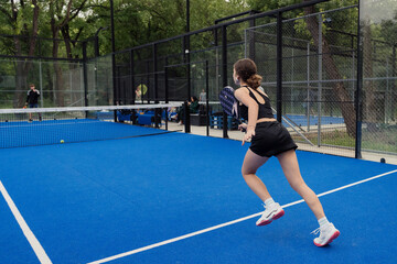 Obraz premium A female athlete in action playing padel tennis on a blue outdoor court. Other players and nature in the background.