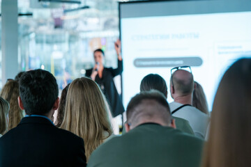 Audience engaged in a business presentation with a speaker using a projector. Professional setting with a focus on learning and information.