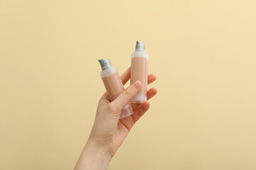 Bottles with foundation in female hands on beige background