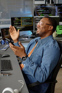 Vertical shot of happy male African American software developer at working desk with multiple screens rejoicing at fixing error celebrating success at office, copy space