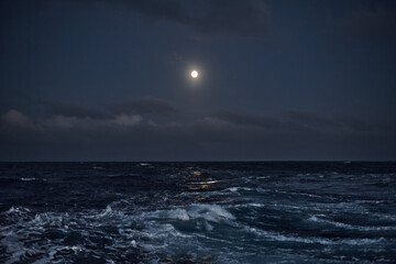 Full moon in the sky over the sea with waves at night.