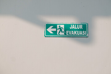Emergency exit symbol attached to the white wall of hospital building, in Indonesian this symbol is Jalur Evakuasi