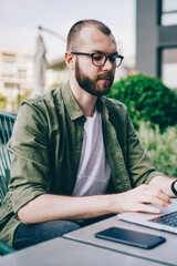 Pensive bearded freelancer searching information on internet websites on laptop device using high speed 4G internet.Young man in casual wear keyboarding information on computer working remotely