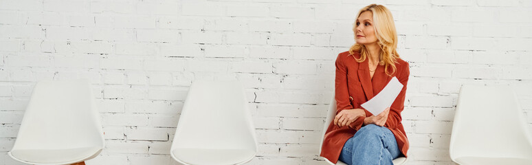 A woman sits elegantly on a white chair in a waiting room.