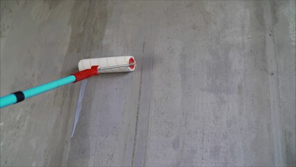The wall is primed with a roller. A man's hand applies a primer to a concrete wall with a roller....